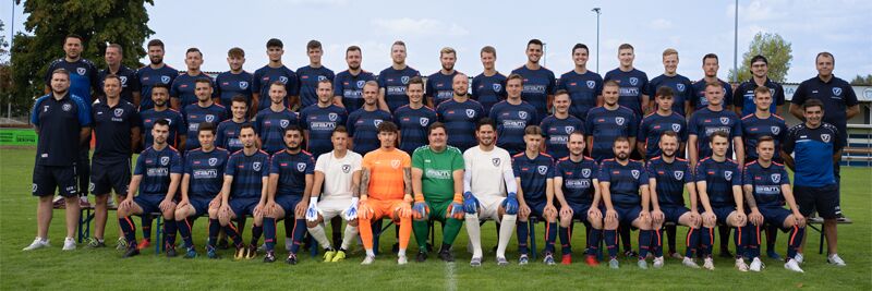 Teamfoto der U18-Mannschaft von FC London, Spieler in Trikots stehen zusammen auf dem Platz, lächeln in die Kamera.